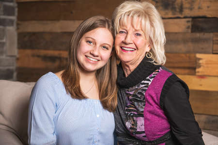 Portrait of grandmother with their teenage granddaughter sitting on sofa at home