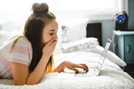 A Young smiling teen girl on bed with laptop