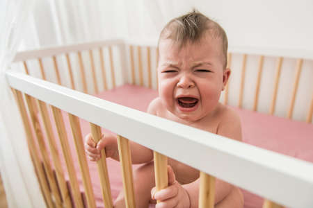 The baby cries and calls mum from a bedの写真素材