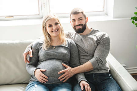 A man embracing happy pregnant woman sitting on couch