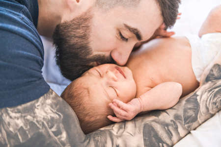 father lay on bed with his newborn baby daughter