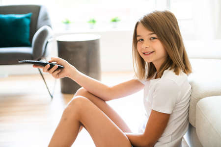 A girl holding remote control and watching TV show