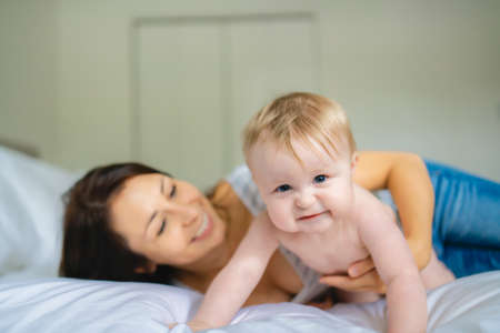 Mother and child on a white bed playing in sunny bedroom