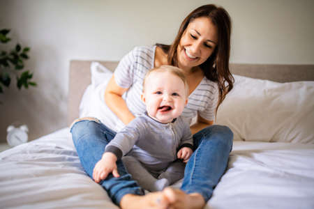 Mother and child on a white bed playing in sunny bedroom