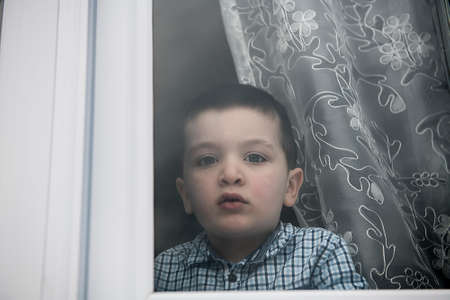 Sad little boy behind a window look sad