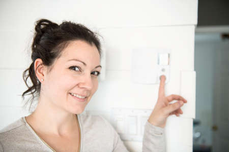 A nice woman set the thermostat at house.の写真素材