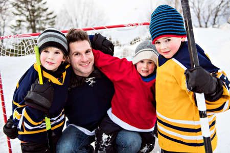 Happy funny kids playing hockey with father on street in the winter seasonの写真素材
