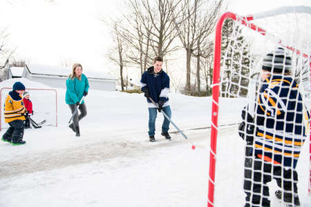 Happy funny kids playing hockey with father and mother on street in the winter season