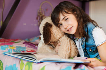 7 years old girl reading a book on bedの写真素材