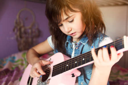 Little attractive girl with his guitar on his knees on the bed in the roomの写真素材