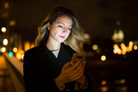 young handsom caucasian woman holding a smartphone on the dark city