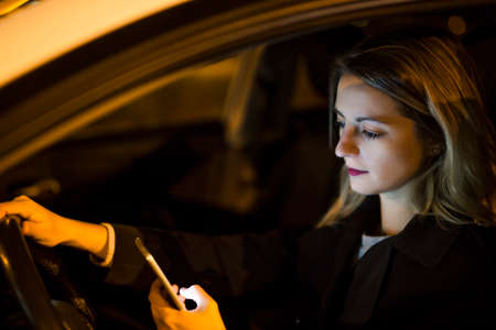 Pretty young woman using her smart phone while driving her car at night