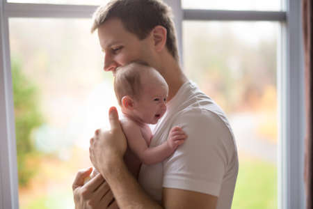 happy family father with newborn baby in front of window