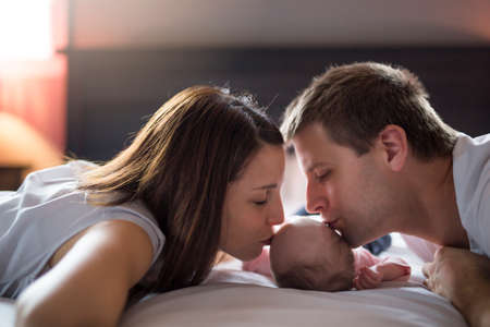 Mother father and baby child on a white bed.
