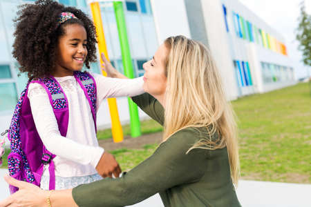 Mother hugging her daughter by school bus outside the elementary school