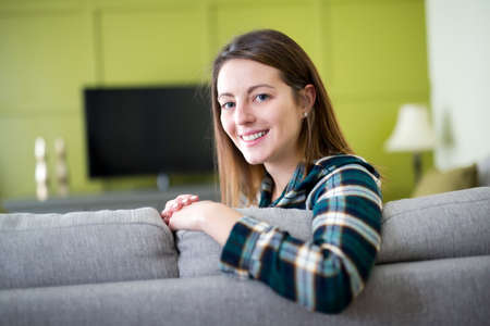 Beautiful woman watching TV sitting on couch at homeの写真素材