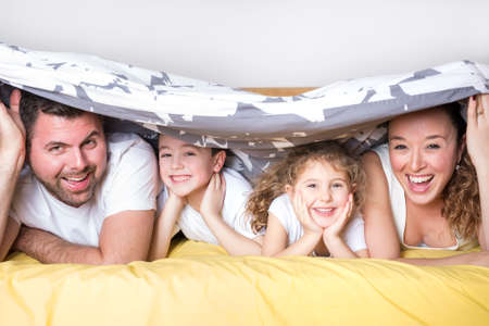 family, children and home concept - happy family with two kids under blanket at home