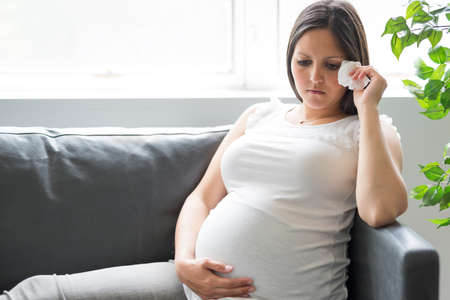 Sad pregnant woman lying on sofa at home