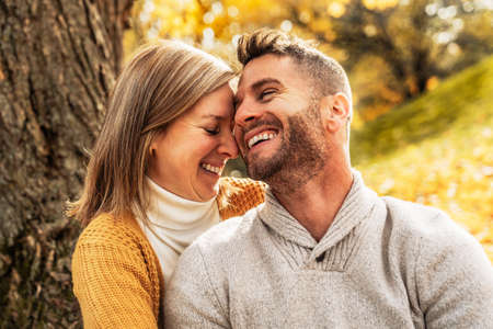 Loving couple in the autumn park sitting on the bottom of a tree