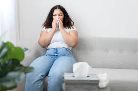 Sick ill black woman with tissue sitting on sofa