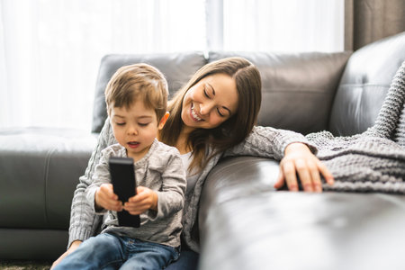 Mother and her son are watching tv while sitting on a couchの写真素材
