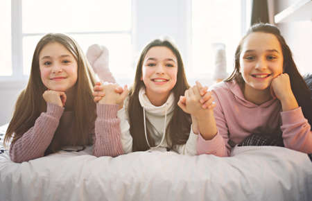 Three excited teenager girls having fun together enjoying laze leisure time on bedの写真素材