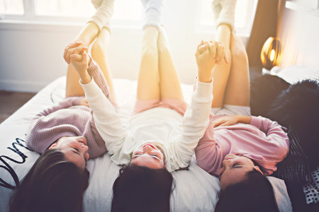 Three excited teenager girls having fun together enjoying laze leisure time on bedの写真素材