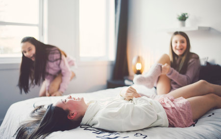 Three excited teenager girls having fun together enjoying laze leisure time on bedの写真素材
