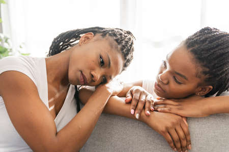 Sad Mother and daughter sitting on sofa at homeの写真素材