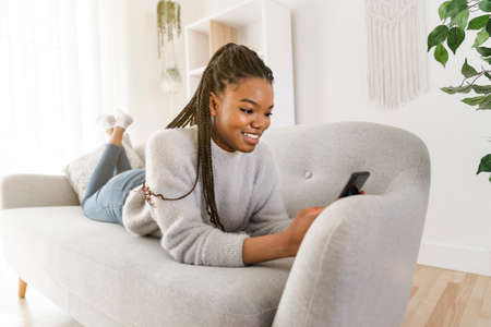 Young African American teen on a sofa in her living room using cellphone