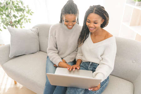 Mother and daughter sitting on sofa at home with laptopの写真素材