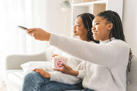 Mother and daughter sitting on sofa at home watching movie with pop-corn