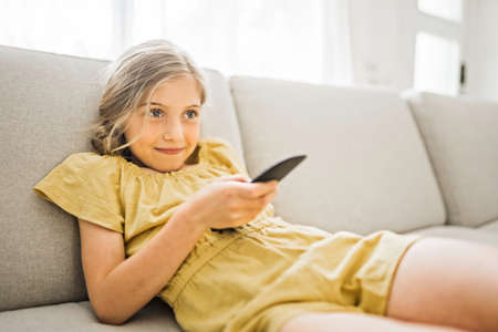 Young girl child sitting on the couch using a remote control