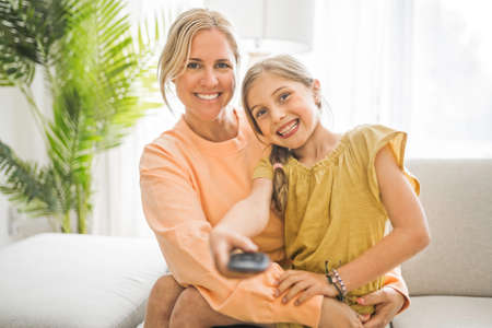 Cute child girl with his young mother at home watching tv