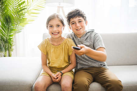 brother and sister sitting on the couch using a remote control