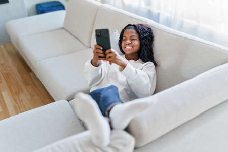 Portrait of a young woman using mobile phone on the sofaの写真素材