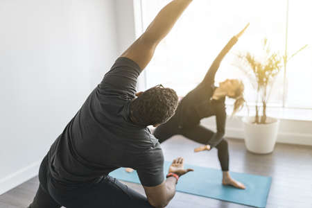 Personal trainer doing yoga pose in sunny studio with client