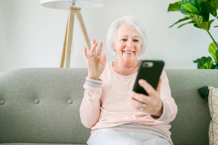 portrait of elderly woman sit on the sofa at home with cellphone