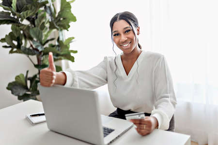 young African American businesswoman working at laptop at home office with credit card