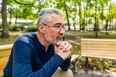 Portrait of a mature man sitting on a bench in an urban parkの写真素材