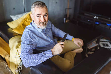 mature man with remote control watching tv at home