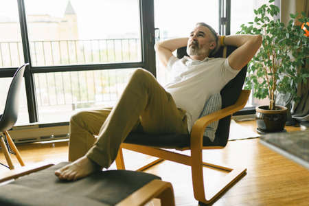 nice Joyful mature man at home appartement with grey beard relaxing on chairの写真素材
