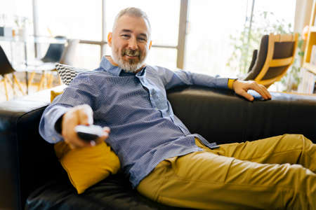 mature man with remote control watching tv at home