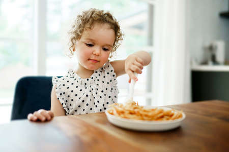 hungry little girl eating spaghetti at home kitchenの写真素材