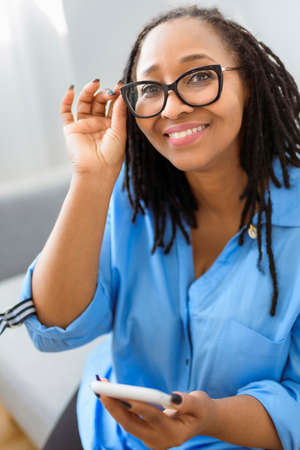 Portrait of an african woman sit on the sofa with cellphoneの写真素材