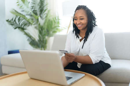 Photo of pretty black woman using laptop at home sofa and buy something on the web
