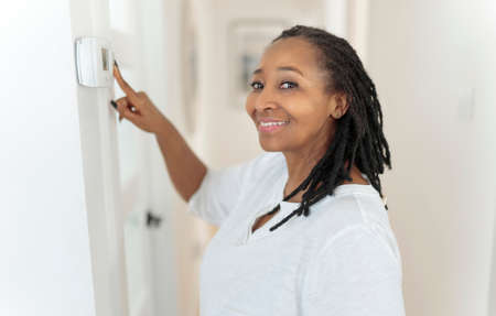 A frican woman lady adjusting the climate control panel on the wall wall thermostatの写真素材