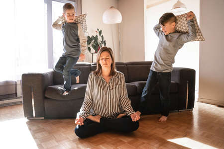 Unhappy Caucasian mom suffer from headache stressed tired by naughty small son playing.