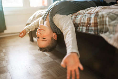 Cute portrait of child upside down, lying on bed, smiling at camera and playing with toy