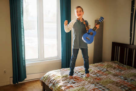 A Cheerful Caucasian boy playing guitar on his bedroom